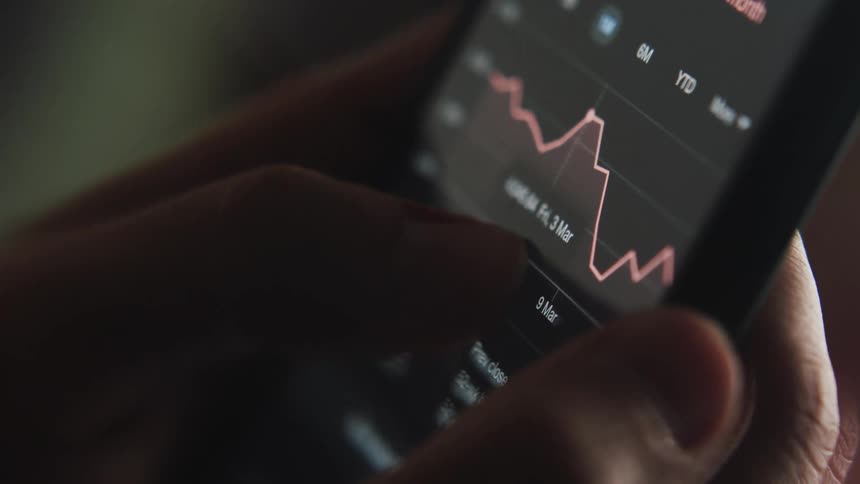A persons hands are holding an electronic device and moving a line on a graph