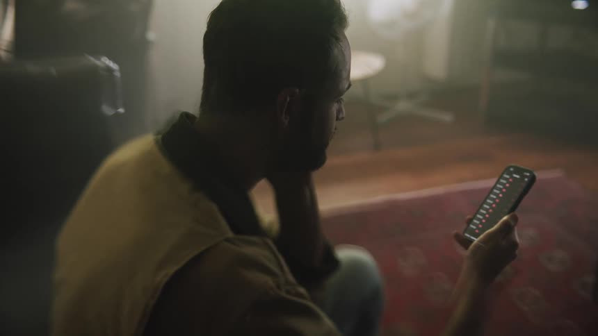 A man nervously touches his face as he scrolls through an app on his smartphone