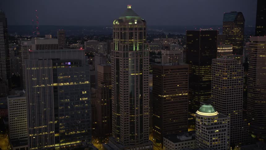 Aerial footage of the 1201 Third Avenue Tower at twilight as a drone approaches and flies by the high-rise building in downtown Seattle Washington