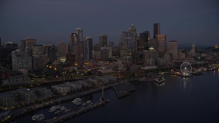  aerial footage of the Downtown Seattle skyline Central Waterfront piers and Seattle Great Wheel passing by during twilight showcasing the high-rise buildings wharf cityscape and industrial harbor of the city - Washington State Aerials