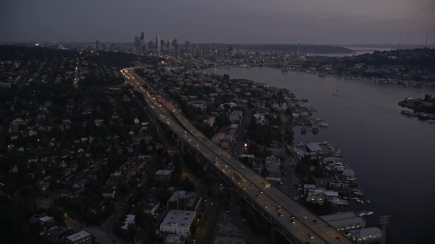 an aerial view of Downtown Seattle skyline and Ship Canal Bridge at twilight as the camera approaches the picturesque Lake Union showcasing the beautiful cityscape cloudy skies and the tranquil water body