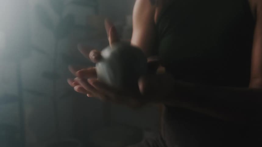 Close up of a sculptor shaping a ball of clay in a dimly lit studio