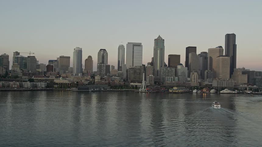 Aerial footage of a ferry sailing towards the Central Waterfront passing by the stunning Seattle skyline during sunset