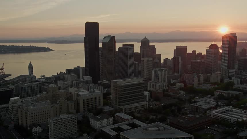 Aerial footage captures the stunning sunset over the high rise skyscrapers of Downtown Seattle with Elliott Bay and the city's vibrant metropolis in the background