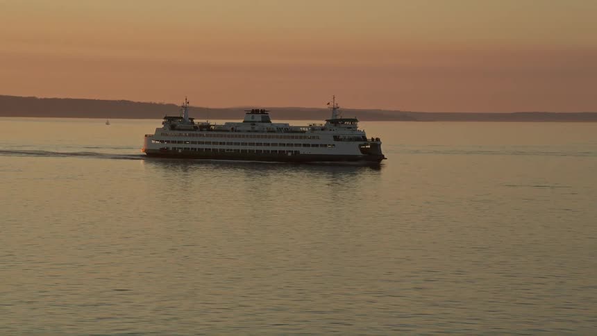 A large ferry boat sails across Elliott Bay in Washington at sunset
