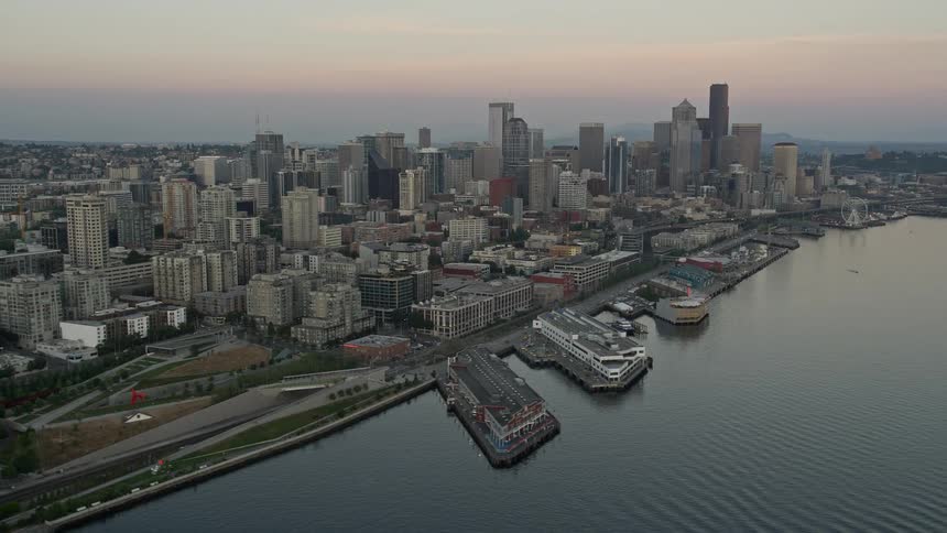 an aerial view of Downtown Seattle at sunset showcasing the iconic Space Needle skyscrapers and Central Waterfront piers with a partially cloudy sky as the backdrop