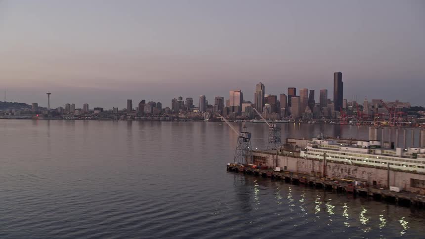 Aerial footage of Downtown Seattle skyline reflecting on the water at sunset with high-rise buildings and skyscrapers lining the coast in the background