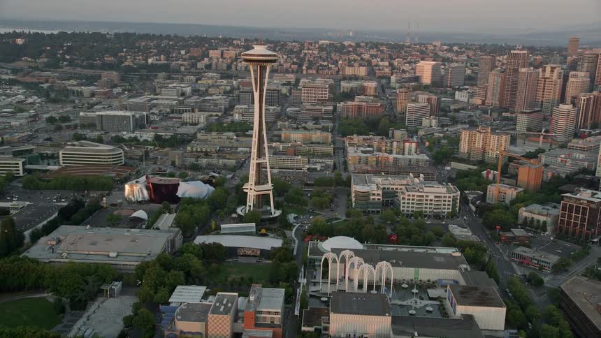 Fly over the shore of Elliott Bay at sunset to approach and orbit the iconic Space Needle in downtown Seattle revealing the city's high-rise buildings and famous landmark