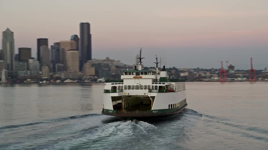 A ferry sails across Elliott Bay revealing the breathtaking Downtown Seattle skyline at sunset in high-quality aerial footage