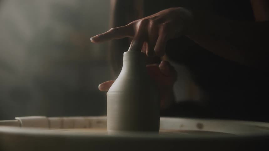 A potter using their hands to sculpt a bottle out of clay on a pottery wheel