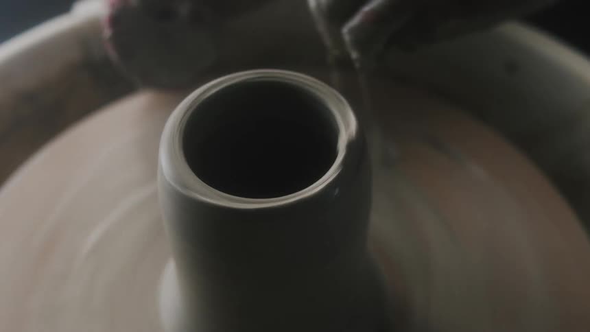 Slurry coats her fingers as woman shapes cup on potters wheel with a soft pad