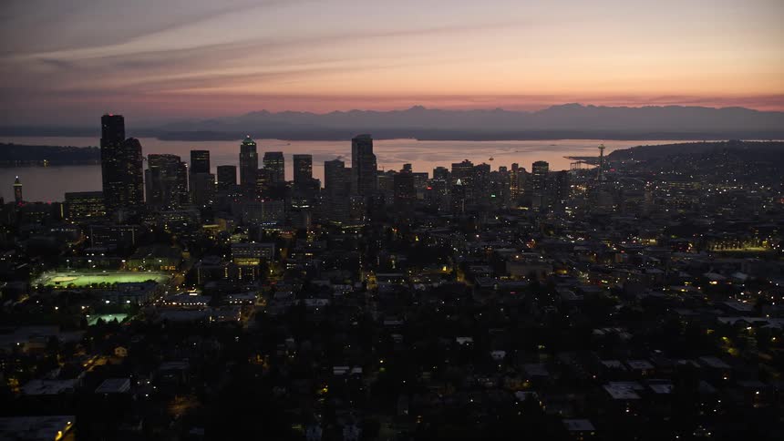 an aerial view of Downtown Seattle at twilight showcasing the city's high rise buildings cloudy skies and the beautiful Elliott Bay in the background