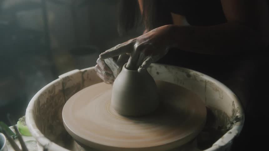 A woman is making clay pottery on a spinning wheel