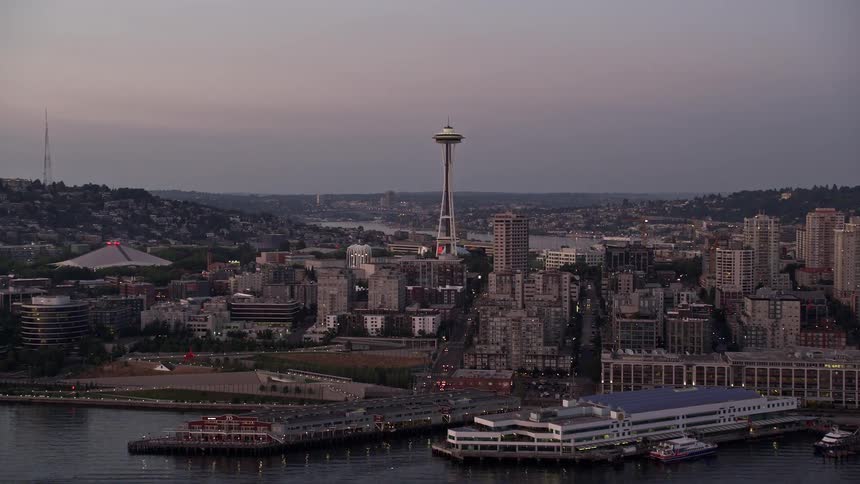 Aerial footage of Seattle's Central Waterfront piers and the iconic Space Needle revealed as the camera tilts up from Elliott Bay capturing the city's downtown area during sunset