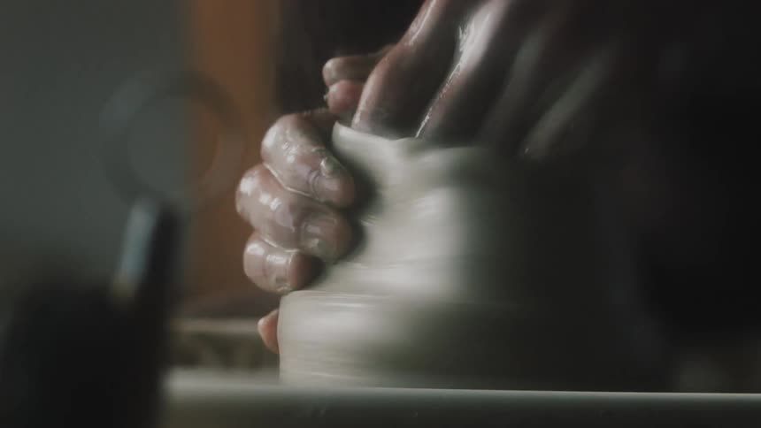 Potter misshapes clay vessel turning on pottery wheel