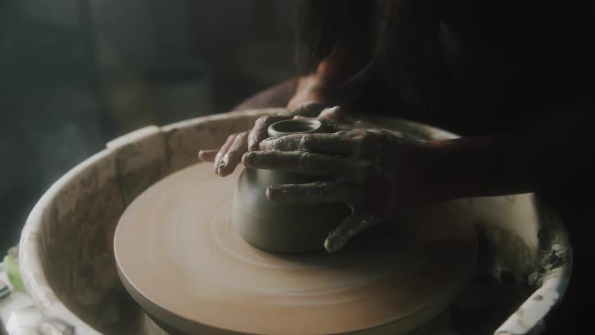 A close up of a person sculpting clay on a pottery wheel as it spins around in their hands