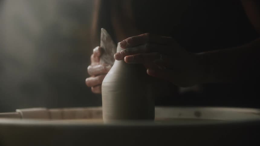 Woman shapes clay vessel spinning on potters wheel with a handheld flat tool