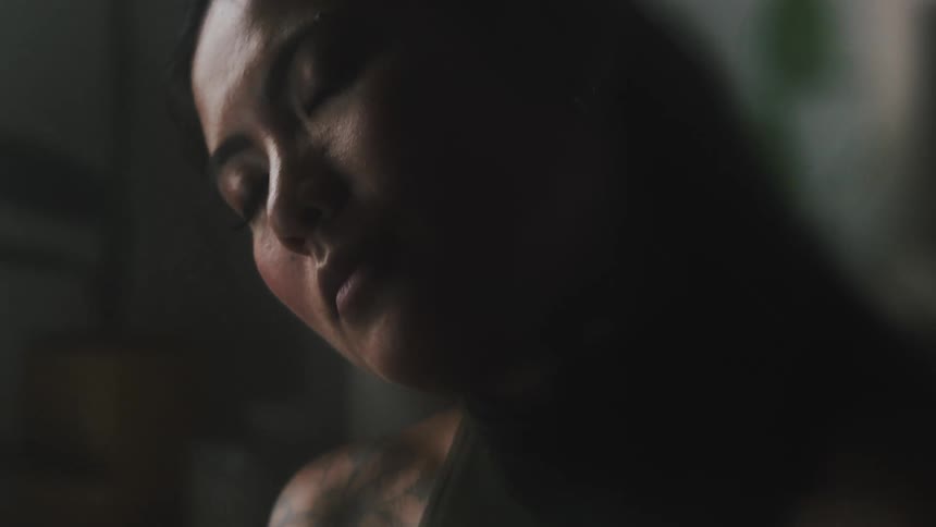 A woman spins her neck to the left and to the right with her eyes closed then stops and opens her eyes with a pensive expression