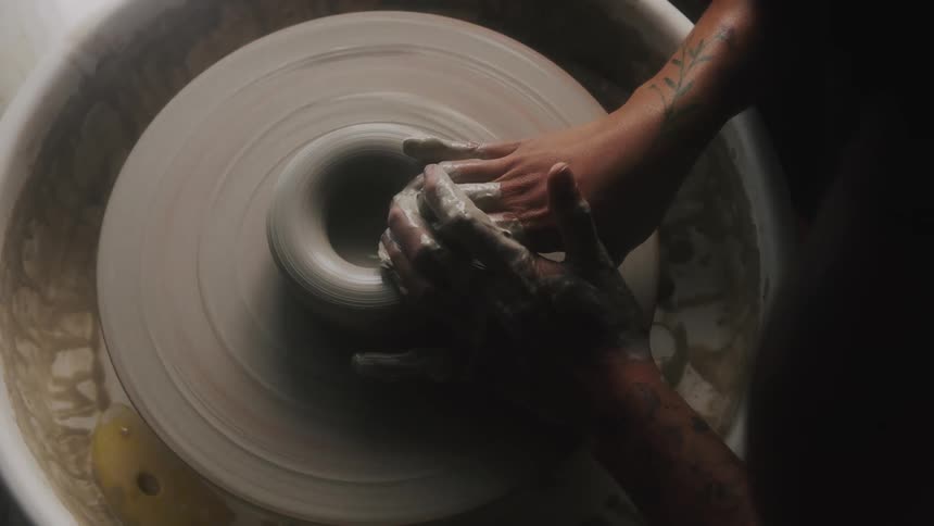 A woman shapes clay on a pottery wheel