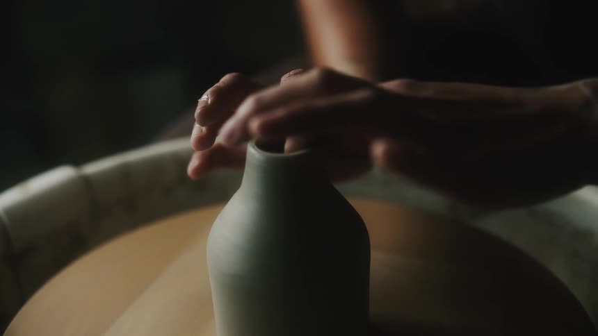 A person creates a vase using a pottery wheel