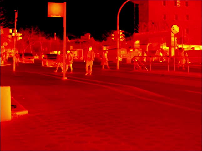 Pedestrians and vehicles move around street at night in infrared image