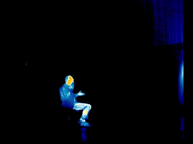 Man sitting in a chair in a dark room with the image distorted and colorful