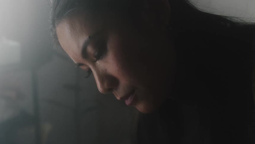 A woman is looking downward in a dimly lit room