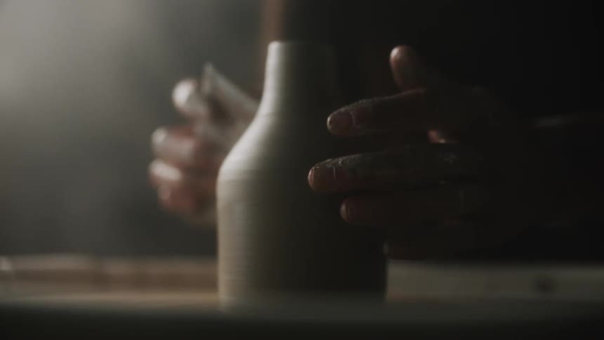 A sculptor uses a tool and a wheel to make a bottle out of clay