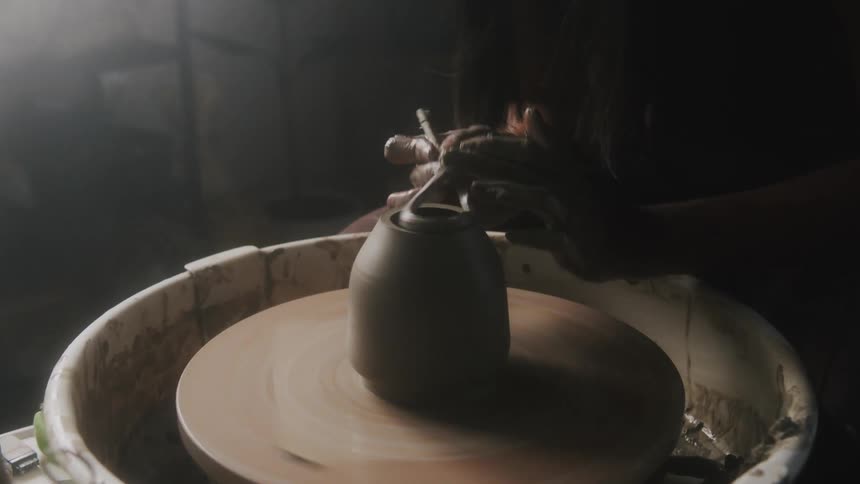 A woman trims the top of a clay vase spinning on a pottery wheel