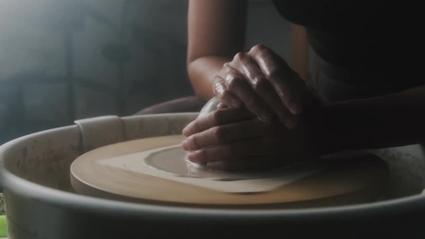 A woman drips water on potters clay spinning on a wheel