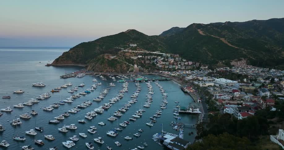 Aerial view of rows of boats moored on the bay in front of a coastal town at morning