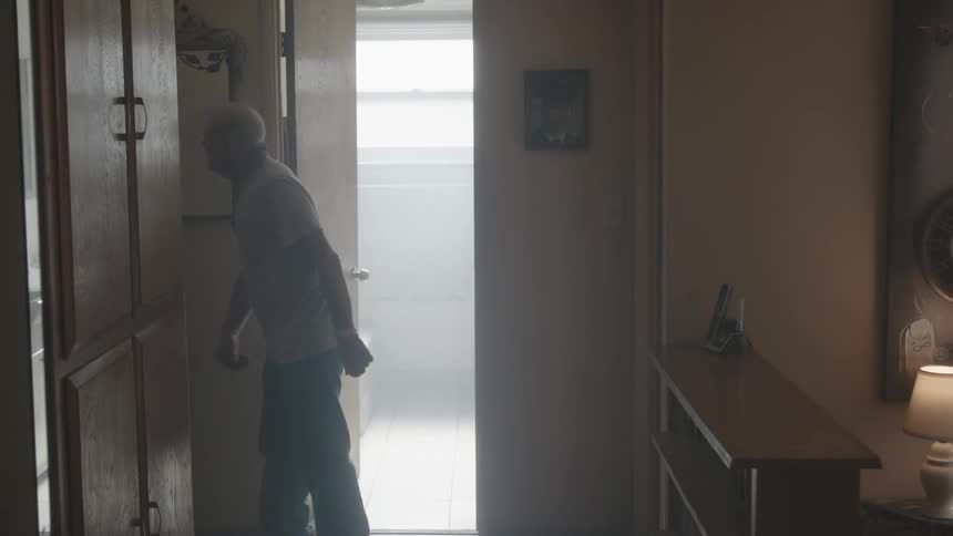 Elderly man stands in dimly lit hallway yelling and angrily gesturing