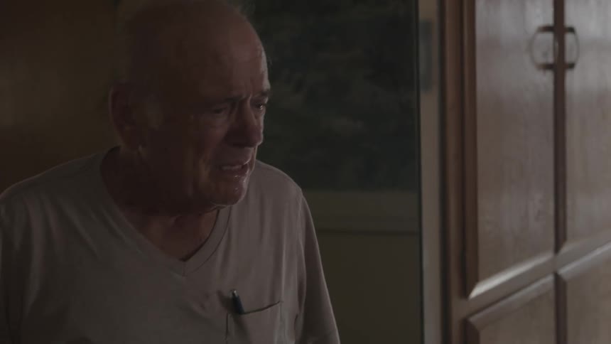 A senior man turns around in the hallway looking sad and walks through his house