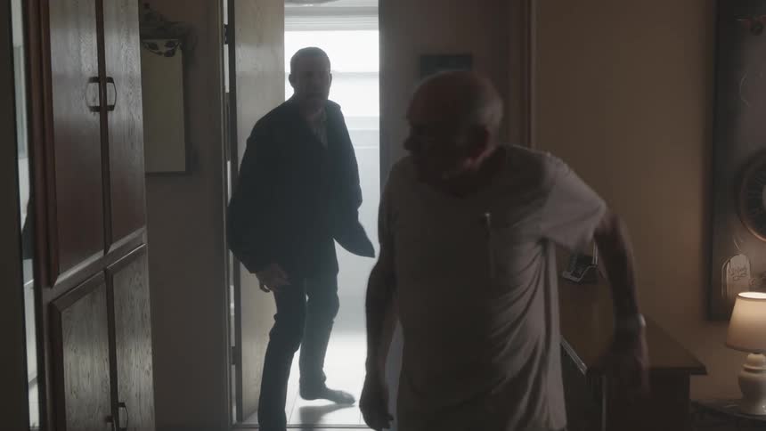 Two man one elderly and the other much younger argue and shout at each other even when the older man is so tired from arguing he has to hold on to a nearby shelf