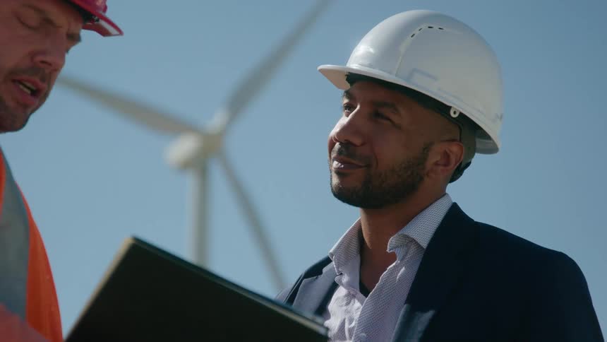 Supervisor talks to a worker near a wind turbine at daytime