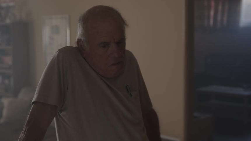 Close up of an elderly tired man standing reclined on the back of a couch at home
