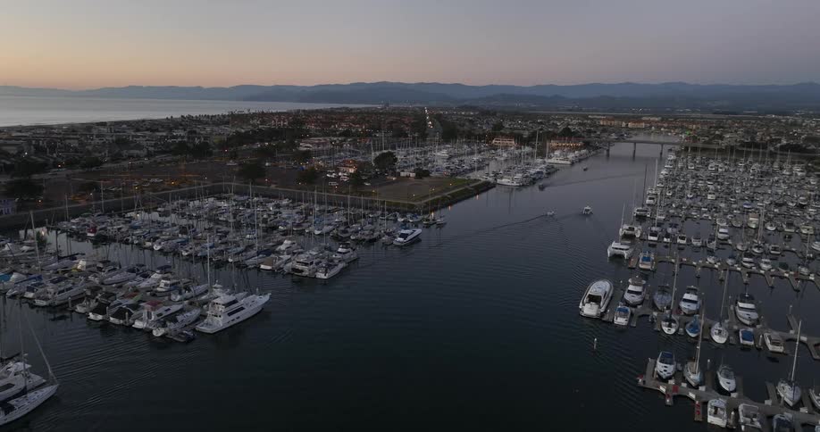 Rows of boats float near channel a short distance from coast with misty mountains under a red sky on the horizon