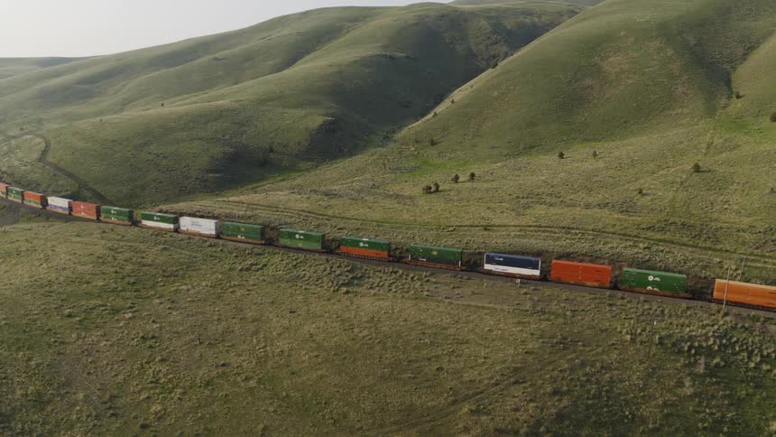Colorful double stacked containers contrast with the landscape as they move through rolling hills