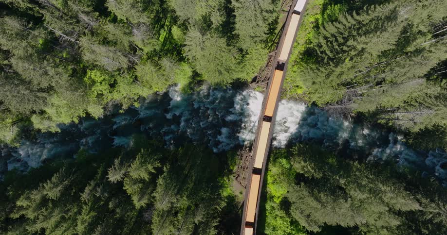 Double stack containers curve around a narrow bridge over a forest river