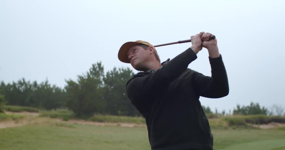 A man standing on a green swinging a golf club during the day probably autumn
