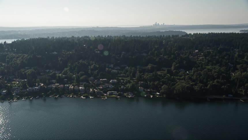Aerial footage of sunlit lakefront homes with individual boat docks on Mercer Island with lush forested areas and a serene lake view in the background
