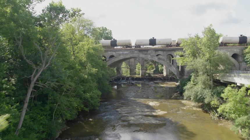 Tank cars travel over a bridge above a fragile river ecosystem