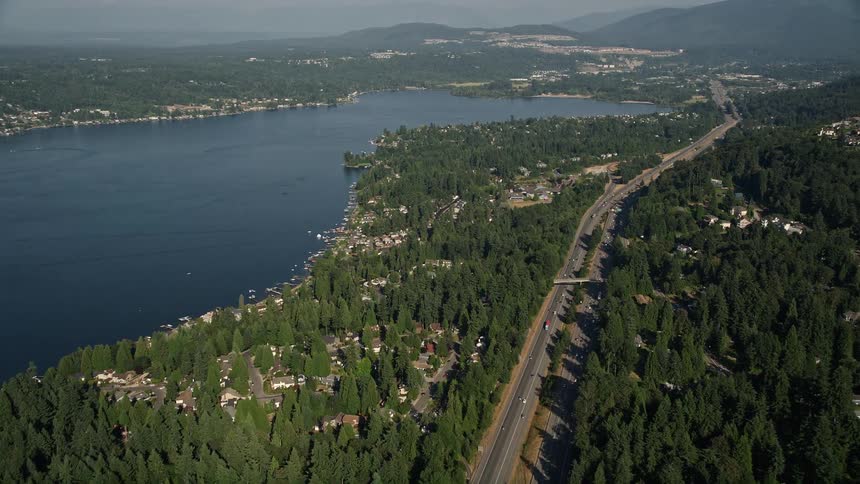 Aerial footage of light traffic on I-90 as it approaches lakeside homes on the shore of Lake Sammamish in Issaquah Washington on a sunny day