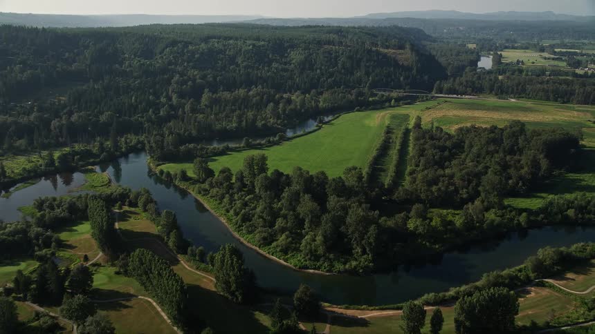 Aerial flyover of a fork in the Snoqualmie River leading to a green field amidst the rustic landscape of Carnation Washington