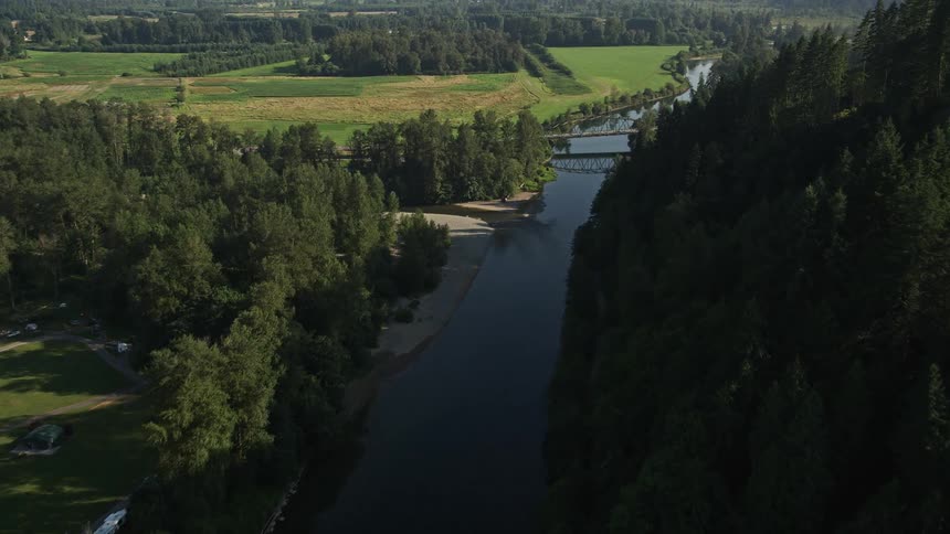 Aerial footage of a bridge over the Snoqualmie River in Carnation Washington with farmland and sunshine in the background