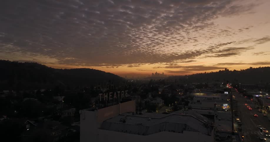 Aerial view of skyline buildings and distant hills are silhouetted against the sky at sunset
