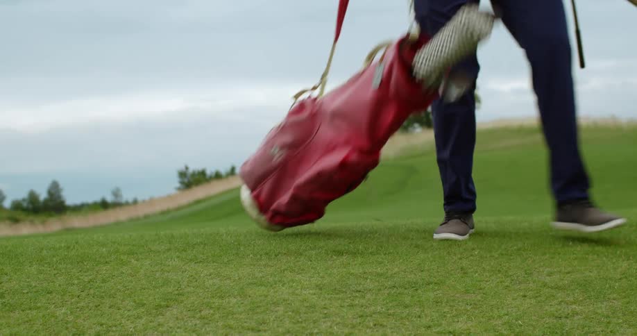 A person goes over a pink golf bag on the ground picking it up afterwards