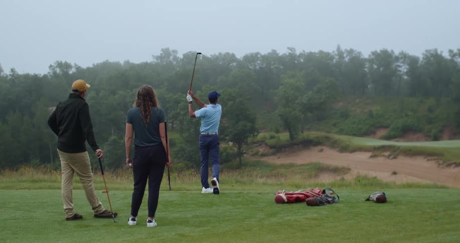 A man and woman watch as another golfer tees off