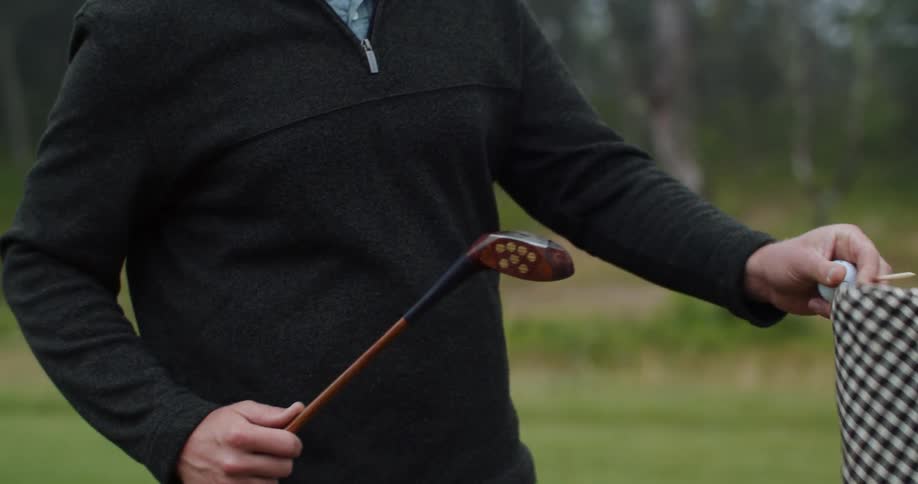 A smiling man takes the protective cover off a golf club