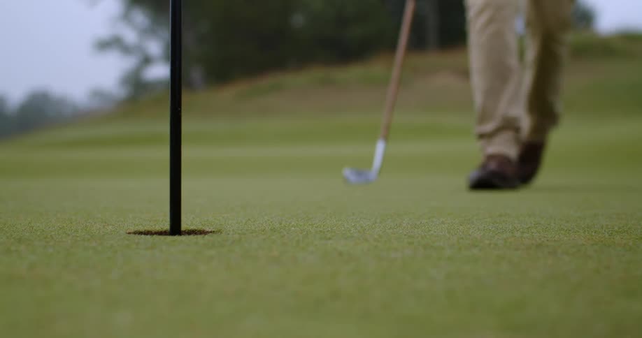 Golfer with brown shoes pants and black shirt plays golf using golf club